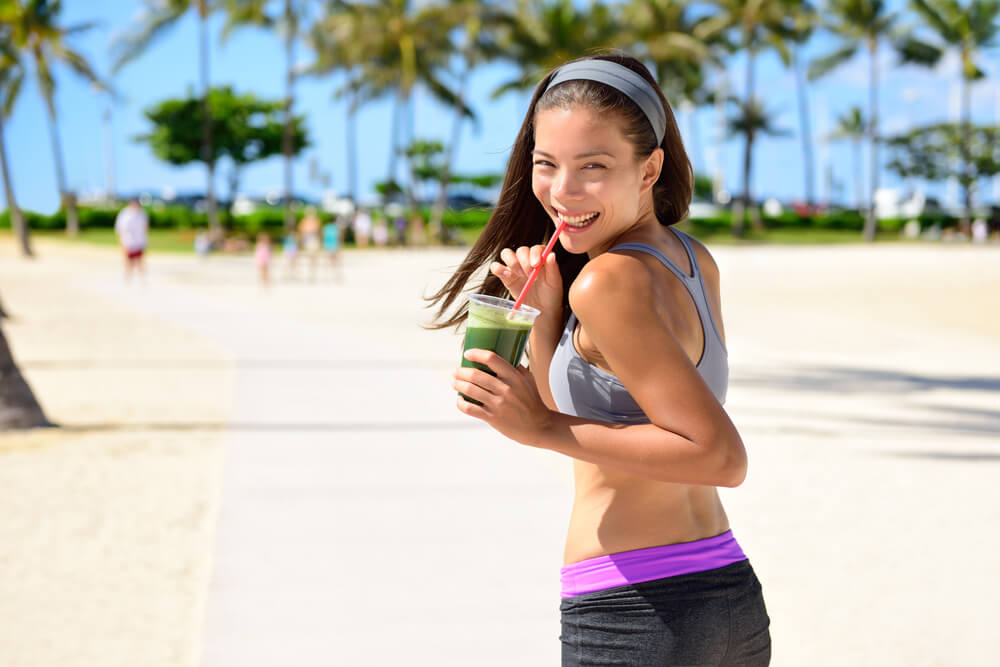 woman walking on pier sipping green juice and smiling