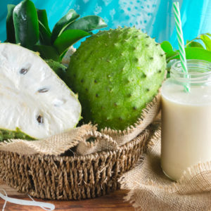freshly cut soursop next to a glass of soursop juice