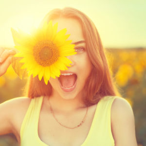teenage girl with sunflower enjoying nature and laughing on summer sunflower field