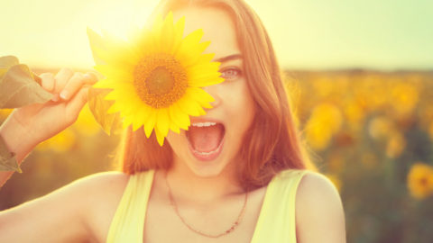 teenage girl with sunflower enjoying nature and laughing on summer sunflower field