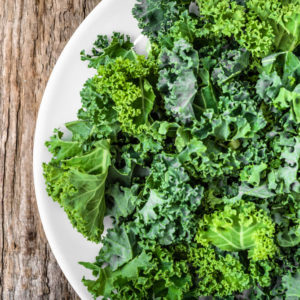 fresh green kale leaves on white plate on wooden background