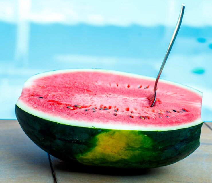 half a watermelon with spoon inside next to pool