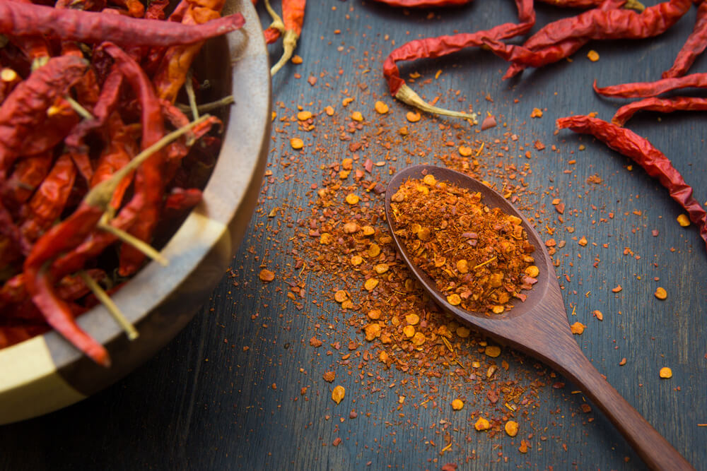 dried cayenne peppers with cayenne powder on wooden spoon