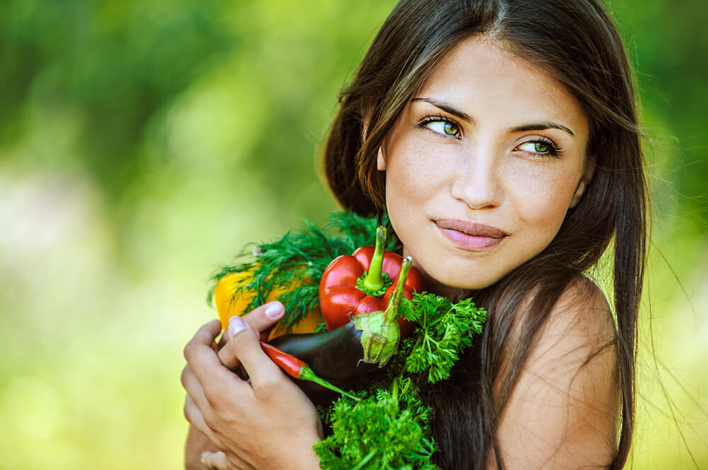 Portrait of young beautiful woman with bare shoulders holding vegetables