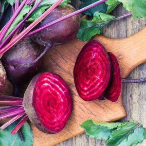whole and cut beets on wooden cutting board with wooden background