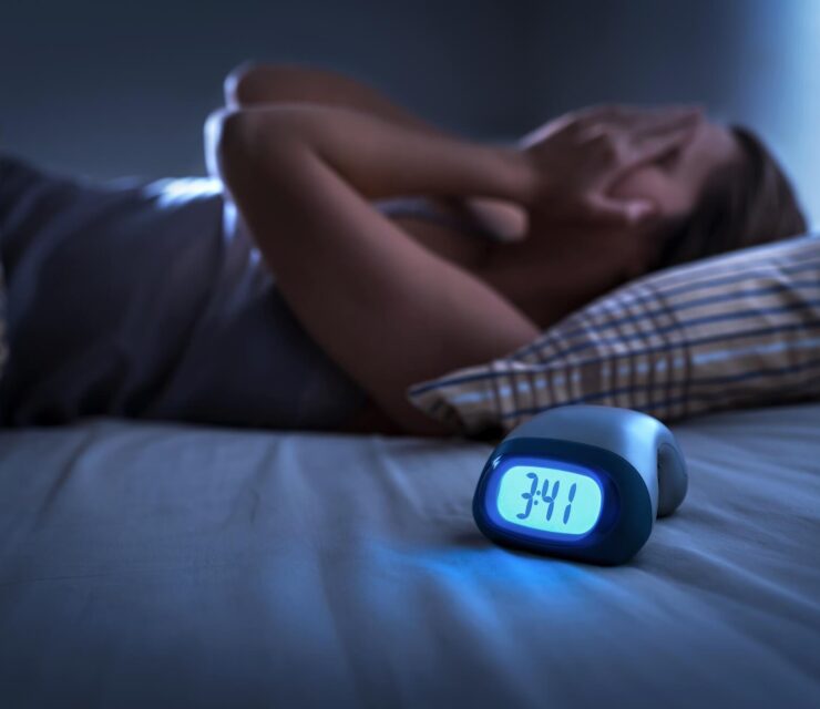 woman holding face in bed, with alarm next to her that says 3:30am in the morning, restless sleep