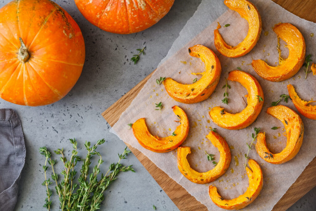 Baked pumpkin slices with thyme on a wooden board over grey table