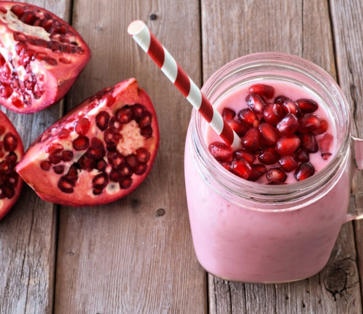 Pomegranate orange smoothie in a jar glass with pomegranate pieces, scene rustic wood