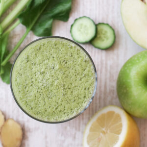 Top view of a glass of organic and healthy green vegetable juice with celery, apple spinach, cucumber, ginger and lemon. Green juice is high in iron, vitamins and essential minerals