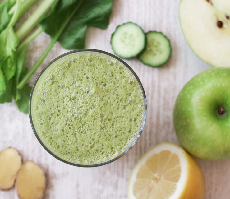 Top view of a glass of organic and healthy green vegetable juice with celery, apple spinach, cucumber, ginger and lemon. Green juice is high in iron, vitamins and essential minerals