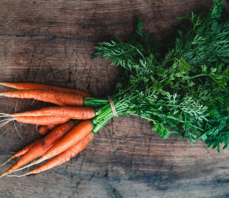 Orange carrots on a wooden background. Bunch of organic dirty fresh carrots with greens close up.