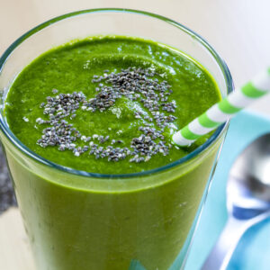 Healthy green fresh fruit and vegetable juice smoothie with blue striped straw and chia seeds heart garnish