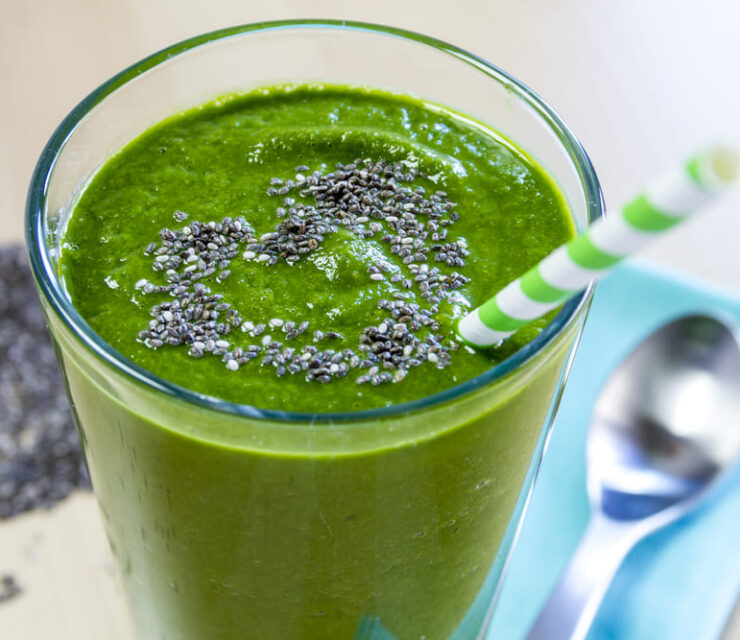 Healthy green fresh fruit and vegetable juice smoothie with blue striped straw and chia seeds heart garnish