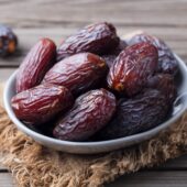 Fresh Medjool Dates in bowl. Grey wooden background. Close up.