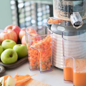 Vegetable and fruit juice healthy with food juicer machine.Woman juicing green and red apple fruits as part of her wellness food or detox smoothie.Cold pressed juice.