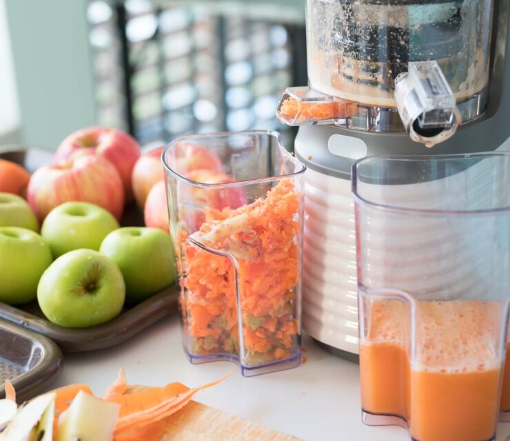 Vegetable and fruit juice healthy with food juicer machine.Woman juicing green and red apple fruits as part of her wellness food or detox smoothie.Cold pressed juice.