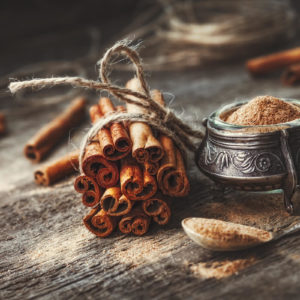 cinnamon sticks wrapped together with string on wooden table next to a small pot and spoon of cinnamon powder