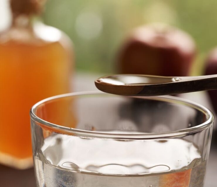 Apple cider vinegar on a wooden spoon above a glass of water