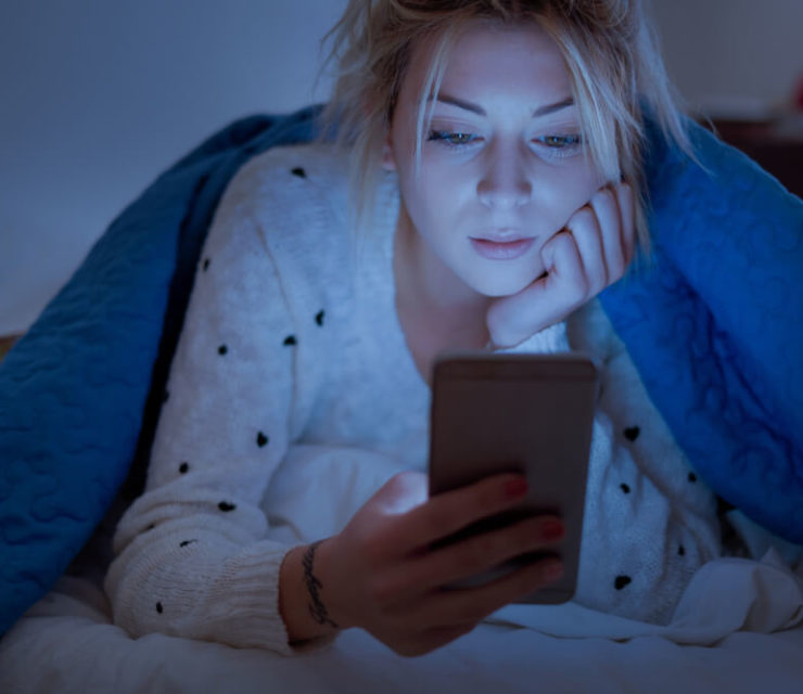 woman holding mobile phone while lying on bed at night