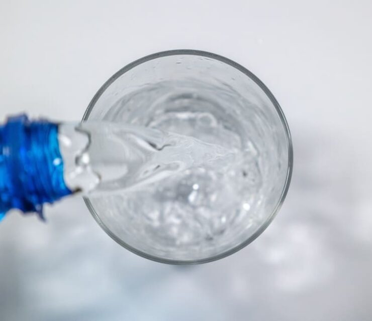 Overhead shot of blue bottle refilling glass with mineral water. Concept: Glass, water, restoration.