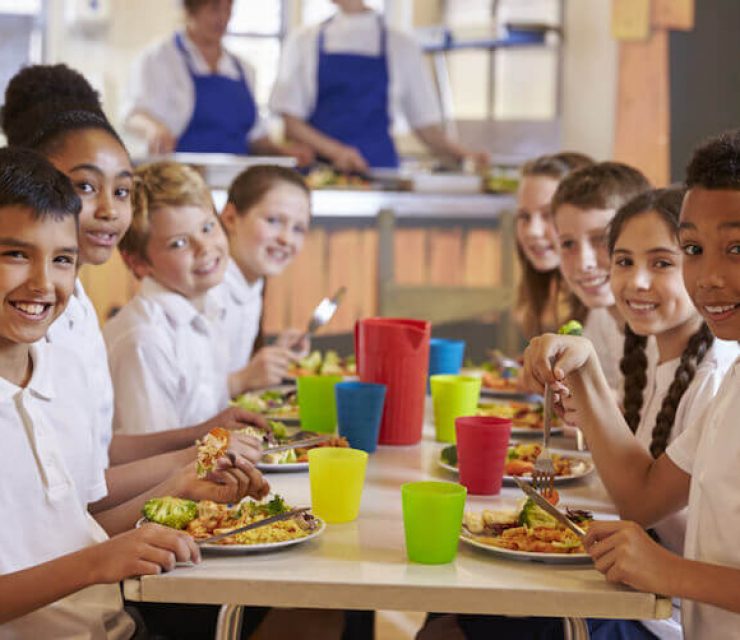 Kids at a table in a primary school cafeteria look to camera
