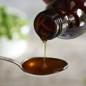 Herbal syrup on a spoon, with fresh Plectranthus amboinicus leaves in the background