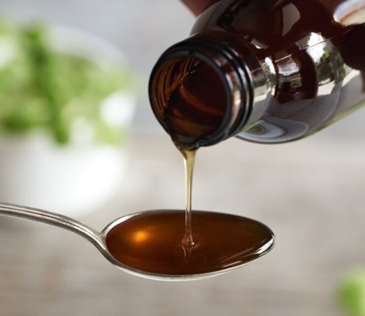 Herbal syrup on a spoon, with fresh Plectranthus amboinicus leaves in the background