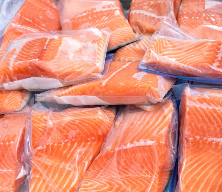 Closeup view of a pile of pieces of raw salmon packaged in small plastic bags on farmers market stand