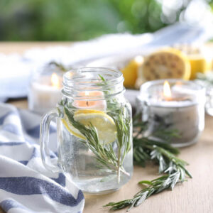 Mason jar with slice of lemon, fresh rosemary and water on wooden table outdoors. Natural homemade repellent