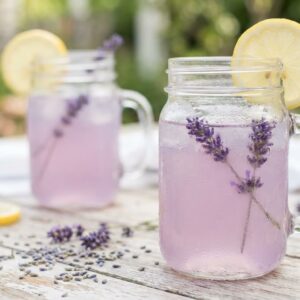 Lavender lemonade in mason jars with lemon slices and fresh lavender sprigs on a bright surface