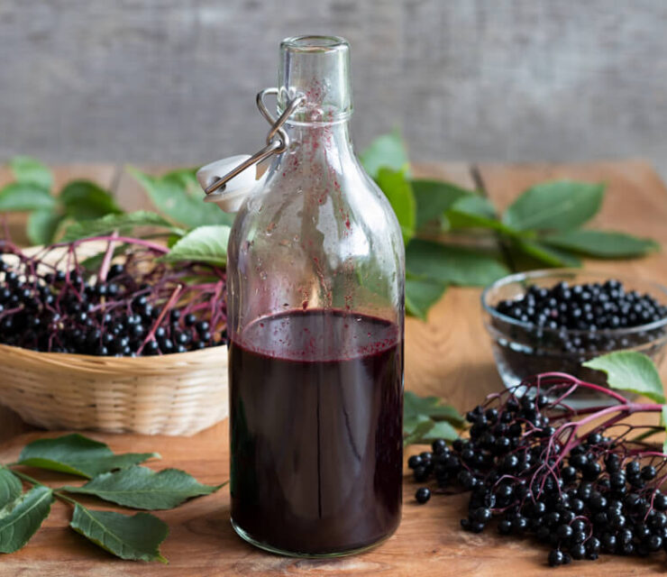 A bottle of elderberry syrup on a wooden table, with fresh elderberries in the background.