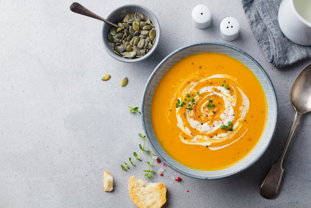 cream of pumpkin soup on grey background with pumpkin seeds in bowl
