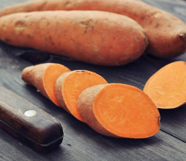 sweet potato on wooden platform with cut slices of sweet potato