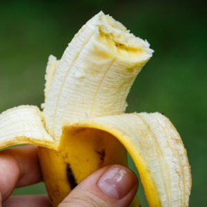 person holding half-eaten banana against green background