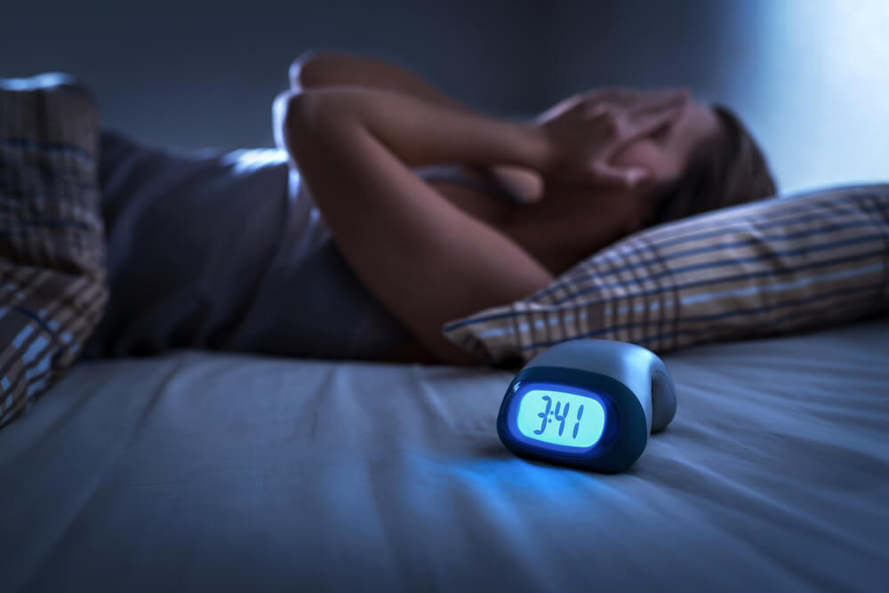 woman with hands on face next to alarm clock 