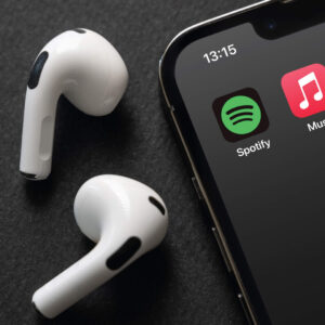 Spotify and Apple Music mobile app icons on the iPhone screen with Airpods next to it