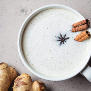 Homemade chai latte with cinnamon, ginger and star anise in a white cup, top view, dark background.