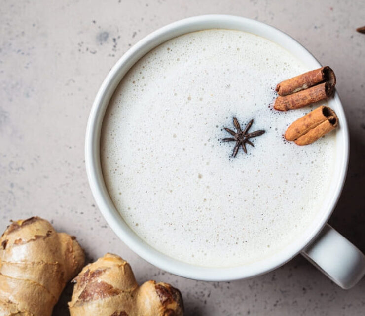 Homemade chai latte with cinnamon, ginger and star anise in a white cup, top view, dark background.